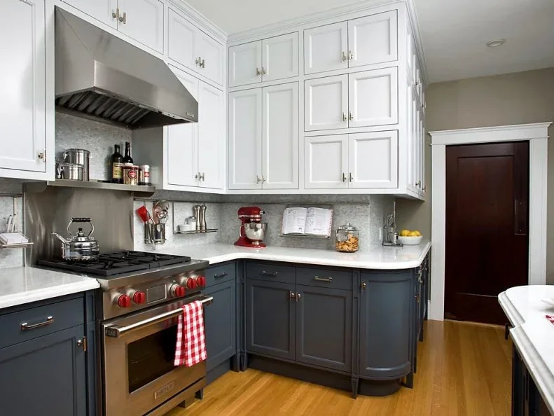 Charcoal lower cupboards and white upper cabinets surround a stainless range, with a pale counter, gray backsplash and wood floor.
