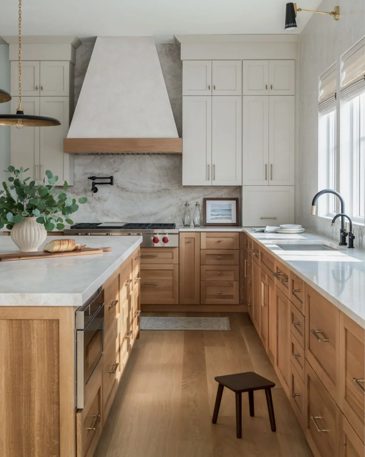 Light wood lower cabinets and an island sit beneath pale upper cupboards and a white hood with wood trim.