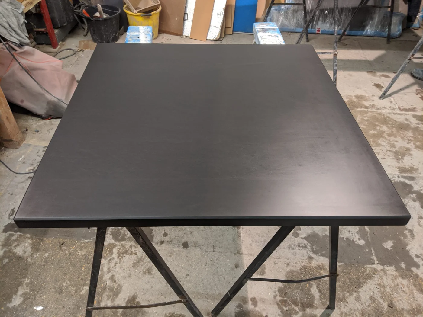 A square honed slate slab with a smooth dark face rests on workshop supports.