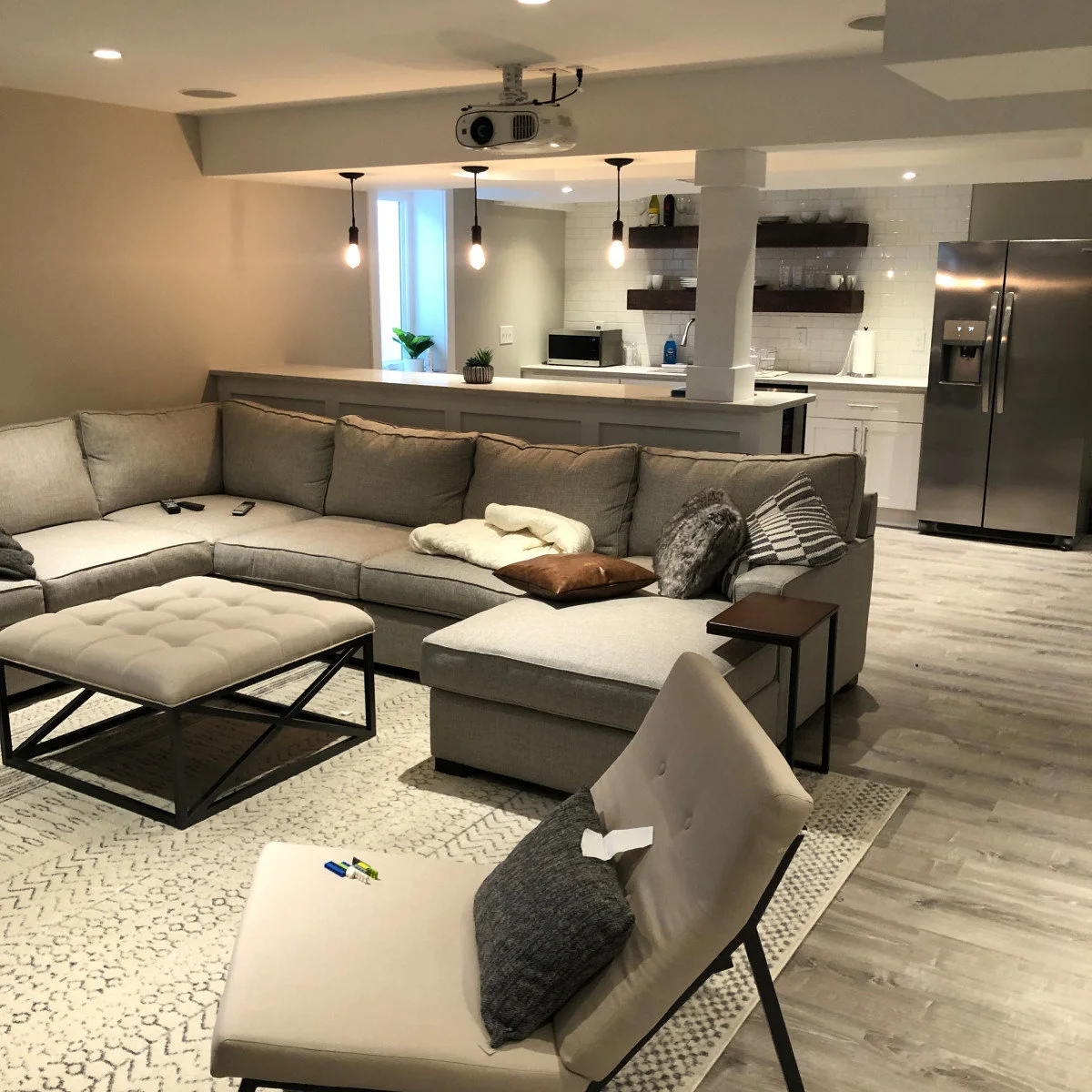 Basement sitting room with large gray sofa and pale bar counter behind it