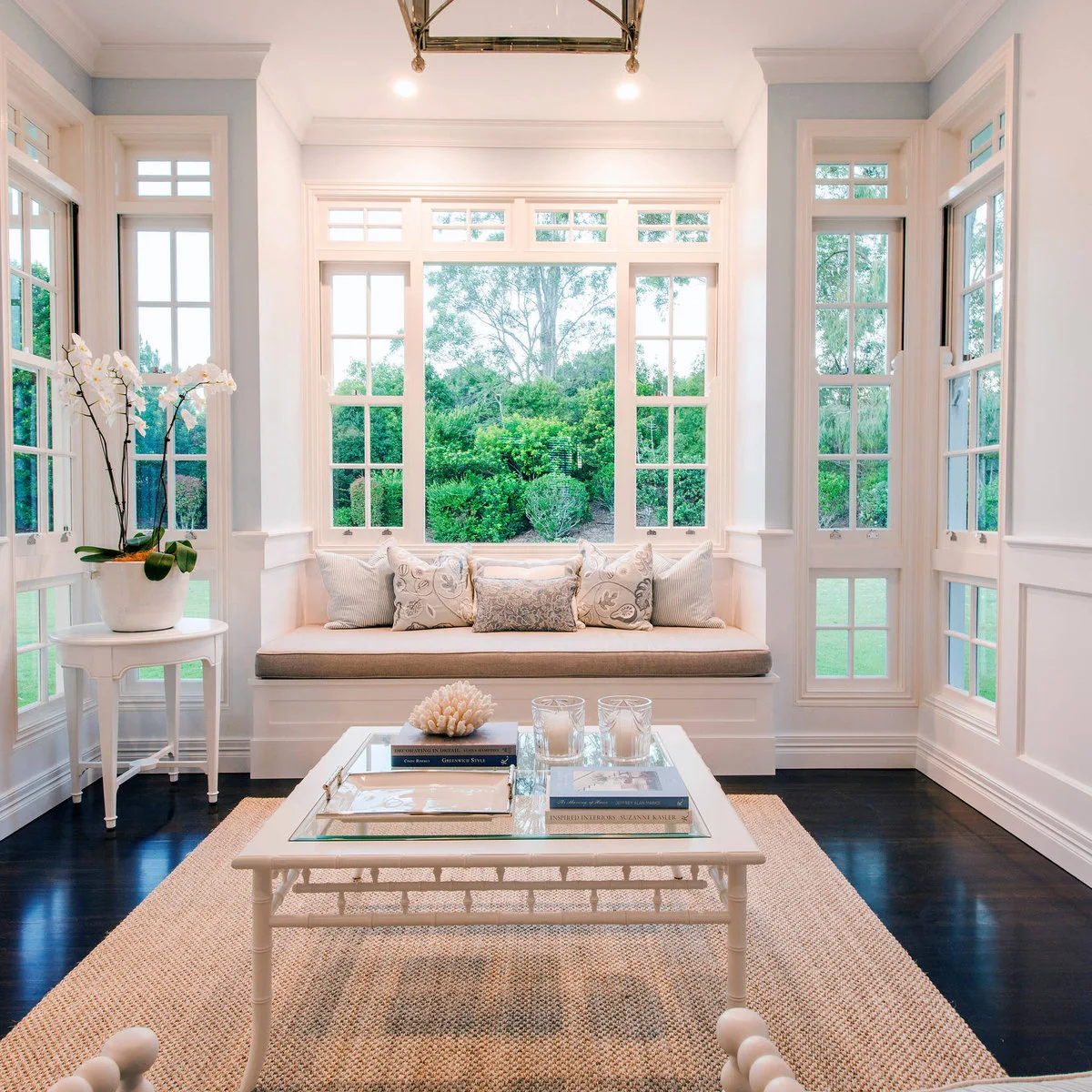 A white box-bay window seat with pale cushions, flanked by tall glazed doors and a glass coffee table.