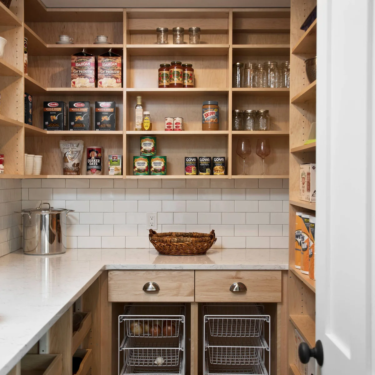 Wood pantry cubbies above a pale counter with wire baskets underneath
