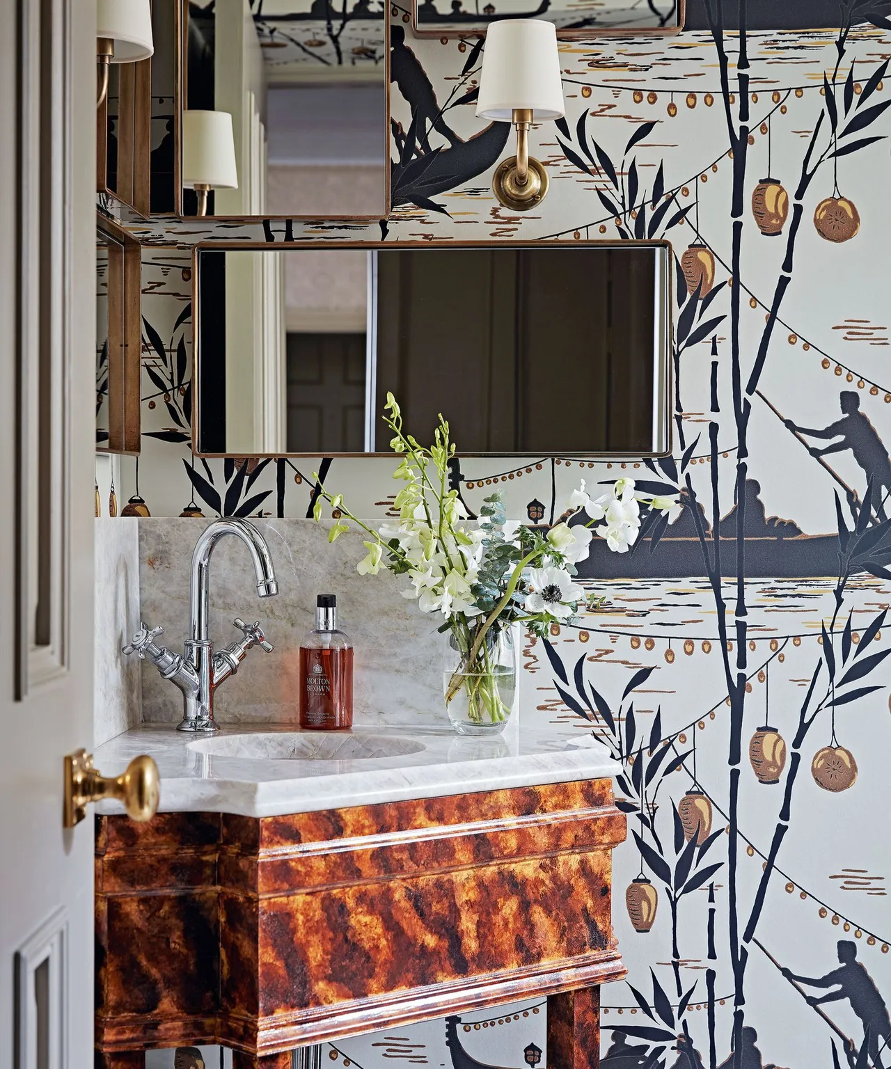Botanical wallpaper surrounds a mirrored basin area above a warm patterned vanity front.