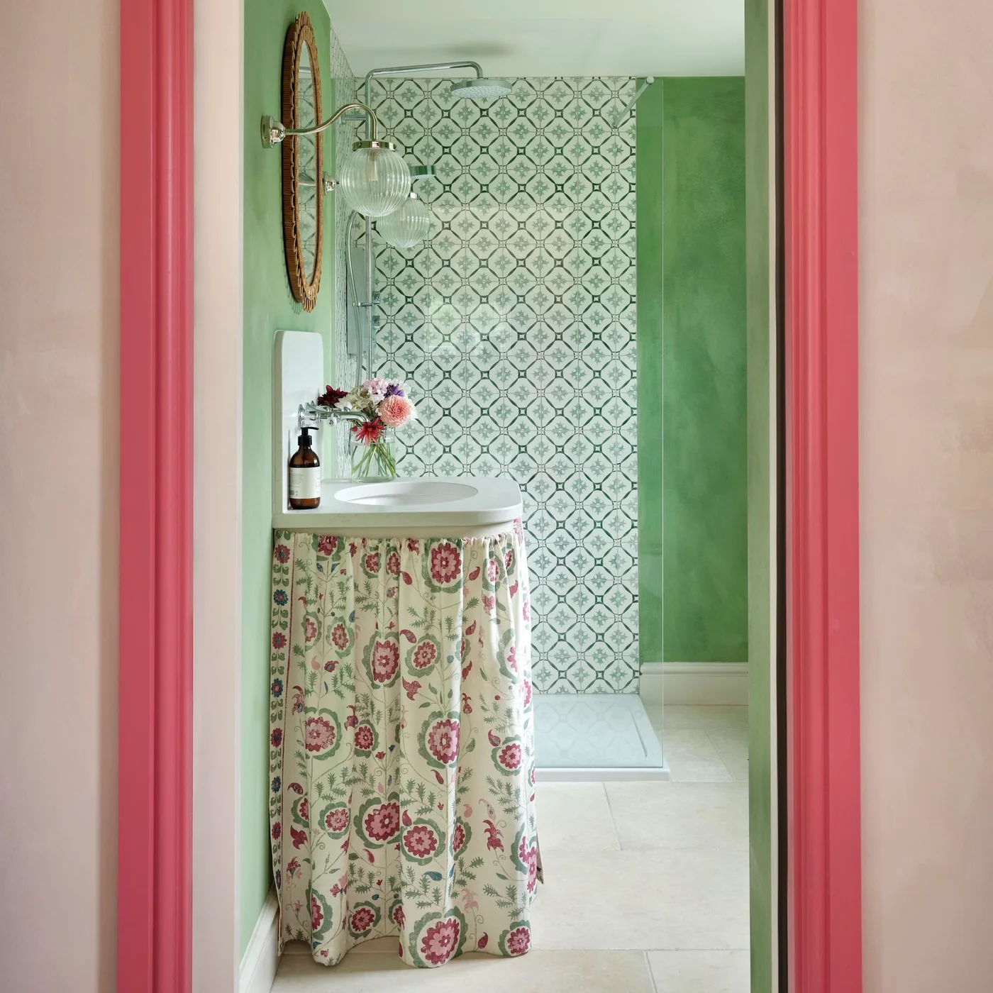 Floral fabric skirt below a wall-mounted basin in a green bathroom with pink doorway trim.