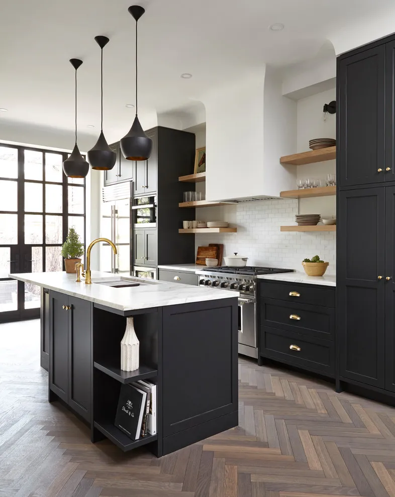 Dark cabinets surround a pale island beside open wood shelves and a bright window