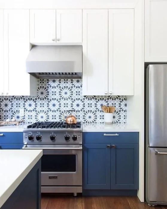 Blue base cabinets and white upper cupboards surround a cooker beneath blue-and-white starburst patterned tiles with a pale hood and metallic appliances