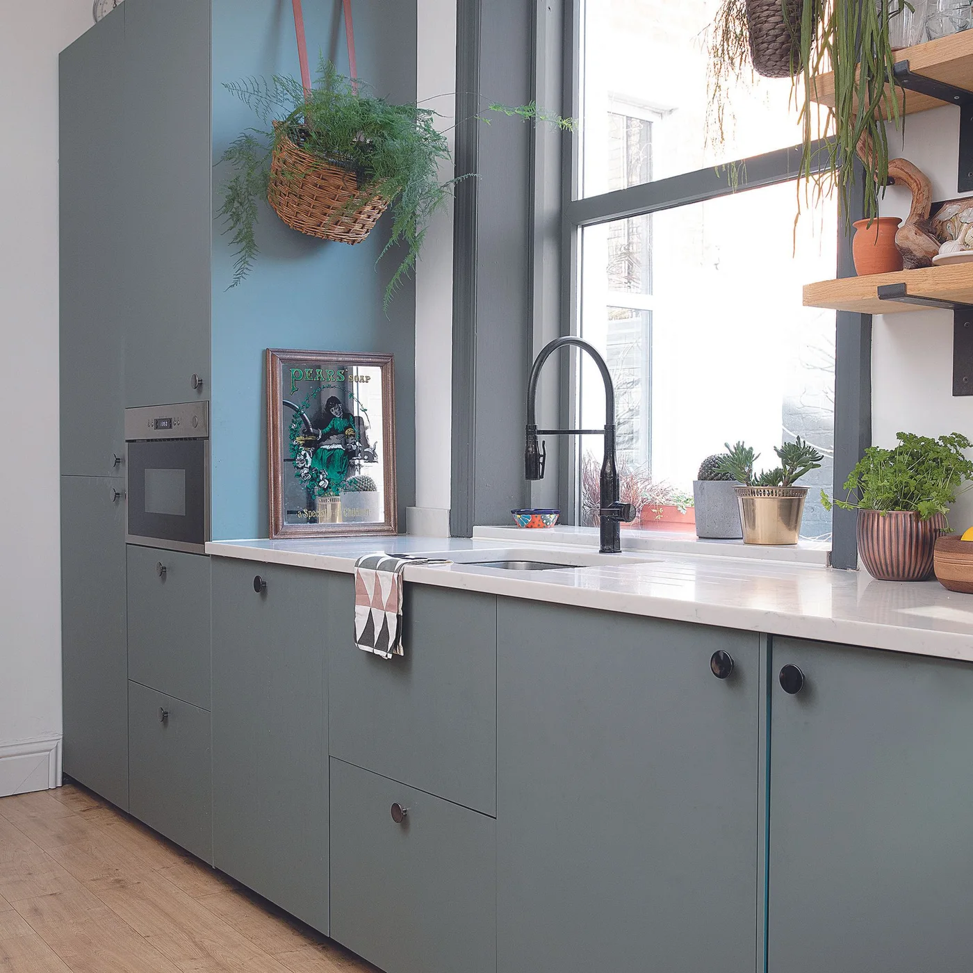 Gray flat front kitchen cabinets beside a bright sink window with hanging woven planters