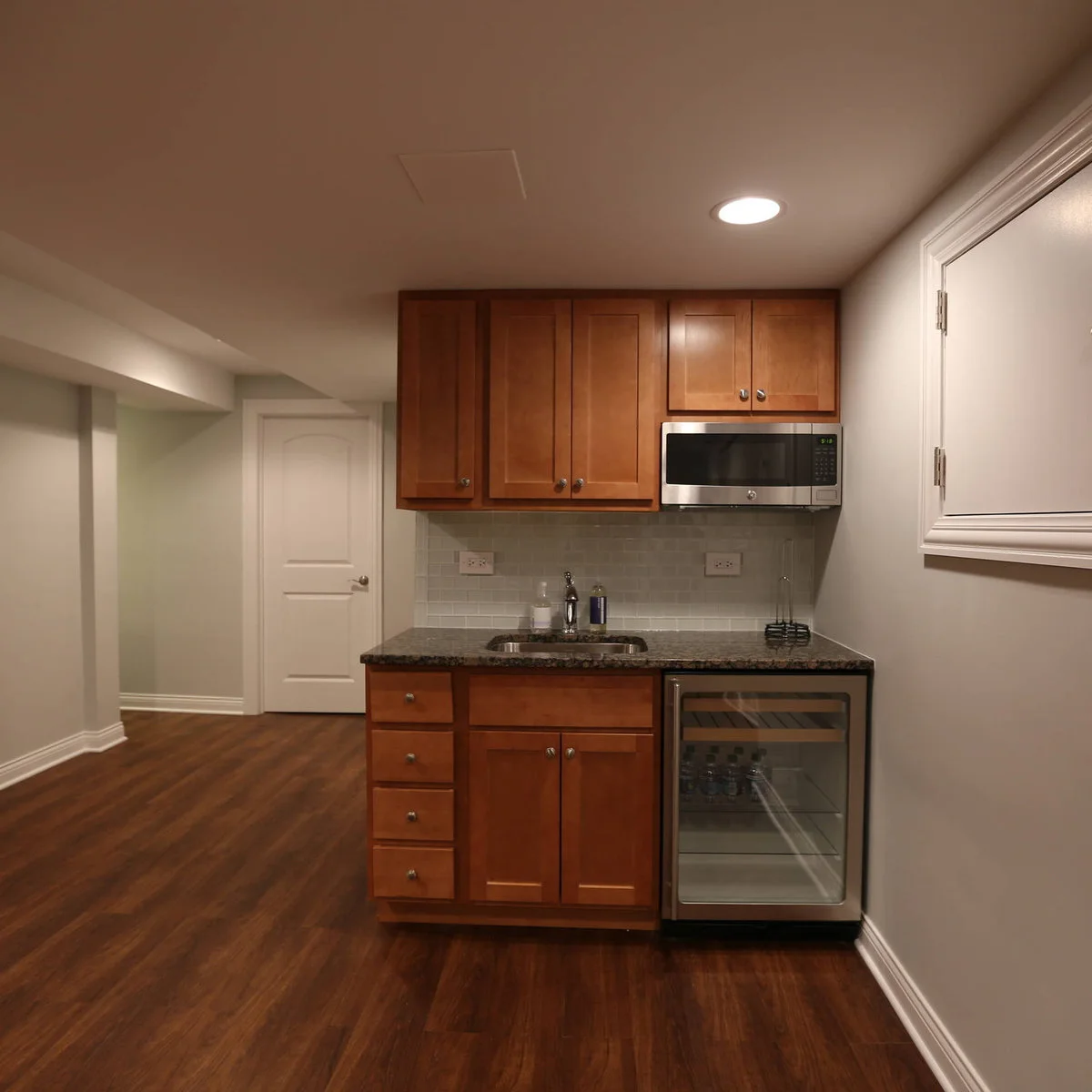 Small wood-cabinet kitchenette with a sink, upper microwave and undercounter glass-front refrigerator