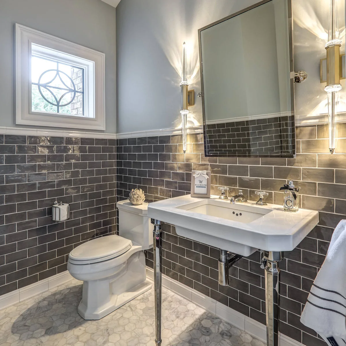 Dark gray rectangular wall tiles around a powder room with a white console sink and narrow vertical lights.