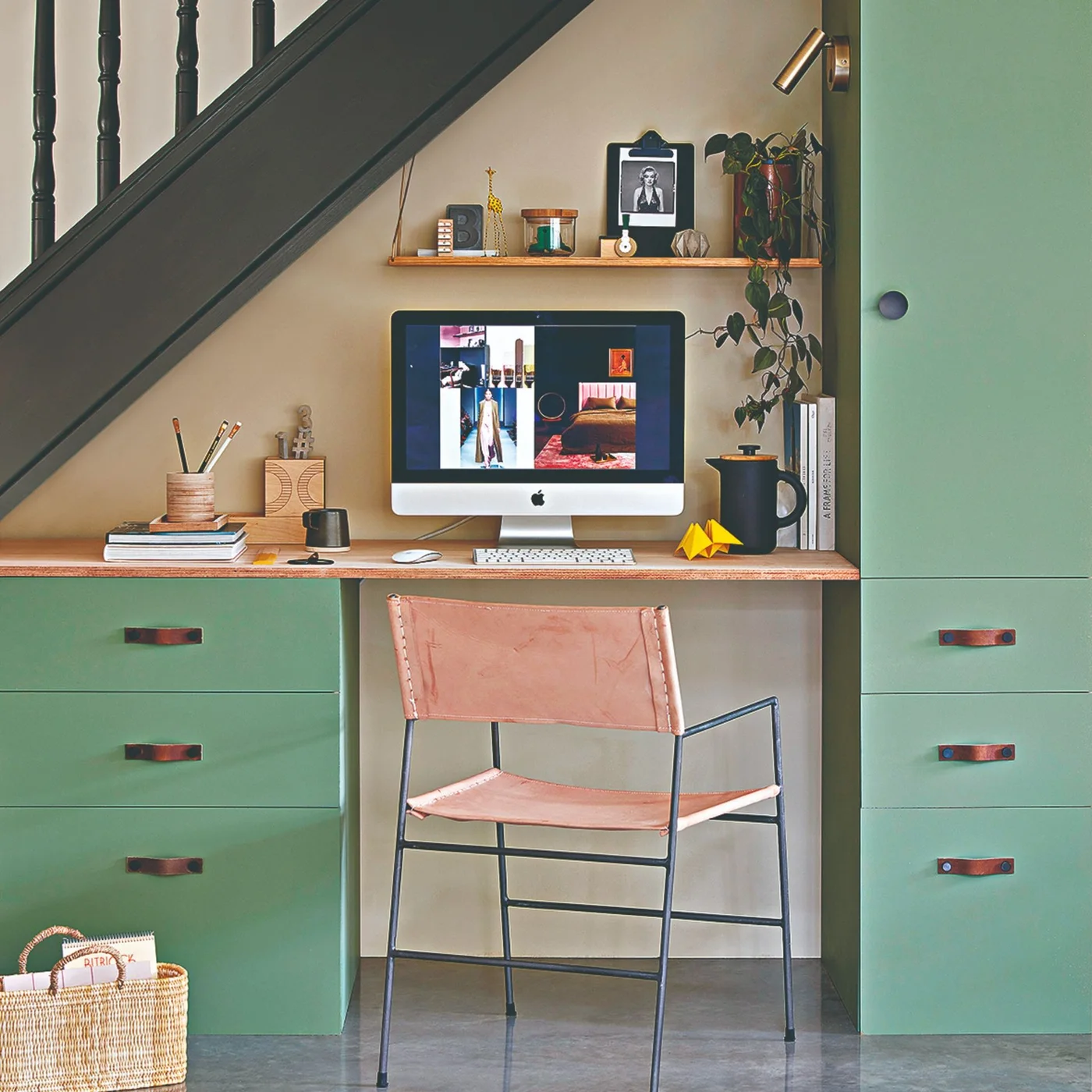 Green drawer units and a tall cupboard frame a wooden desk beneath a staircase beside a pale pink chair