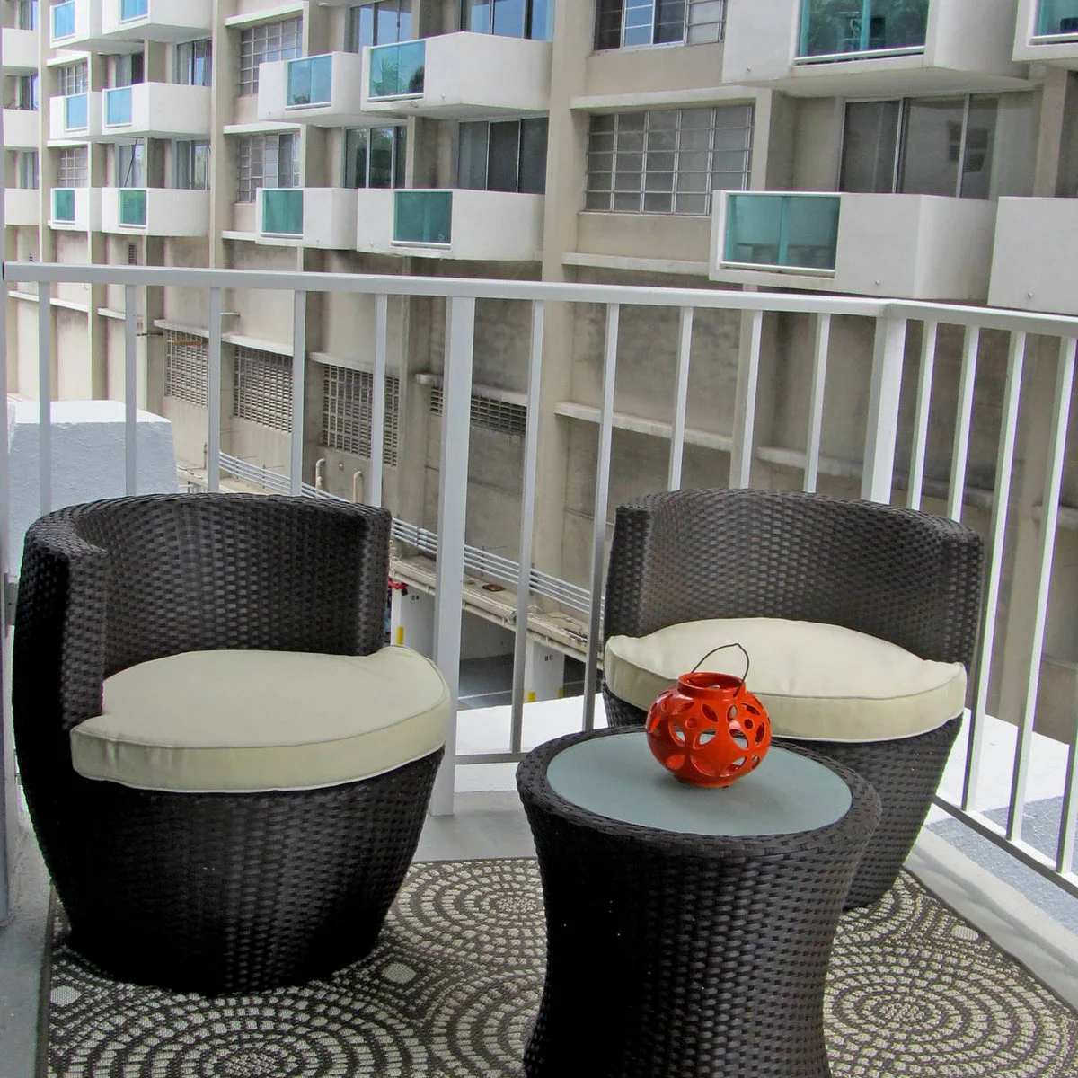 Two dark rounded balcony chairs with pale cushions, a round table and patterned rug