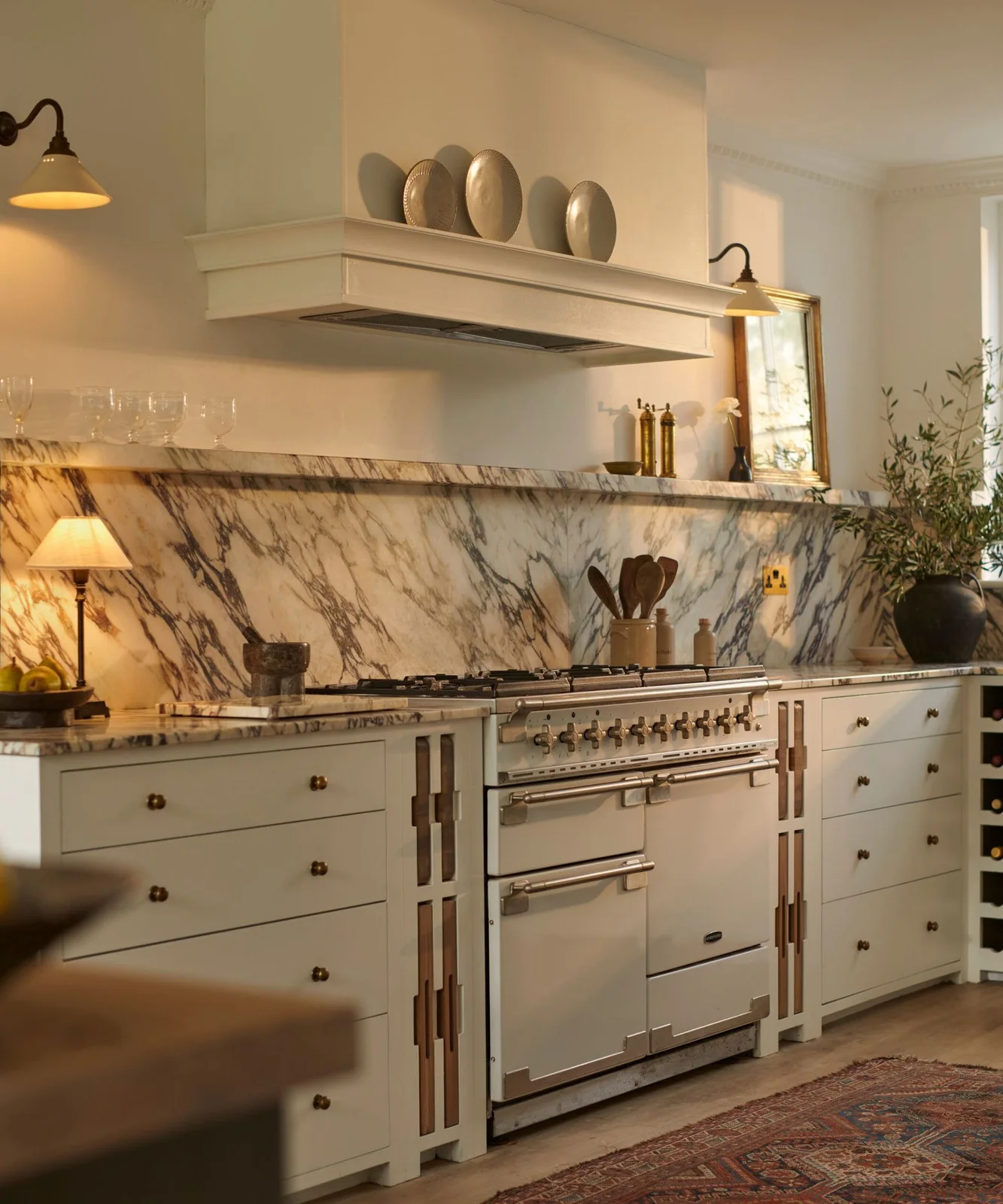 Warm white lower cabinets include narrow open slots beside a range beneath a white hood and veined backsplash.