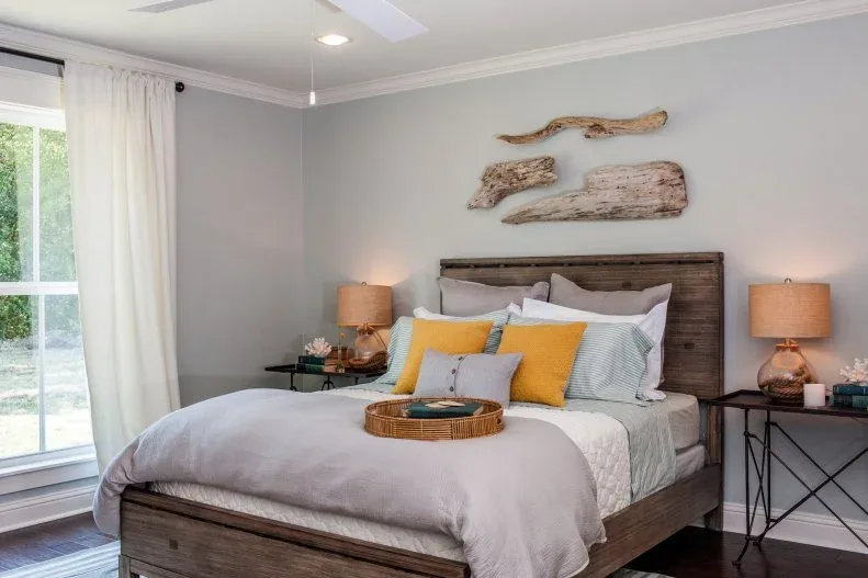 Irregular wood wall pieces above a wood bed with pale bedding, yellow cushions and warm-toned lamps