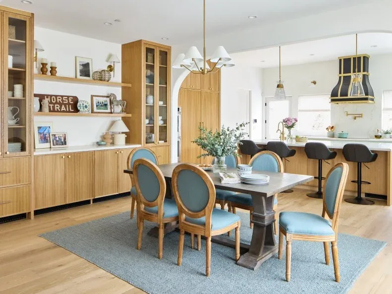 Blue-gray rectangular rug beneath a pale dining table and blue oval-backed chairs beside wood kitchen cabinetry