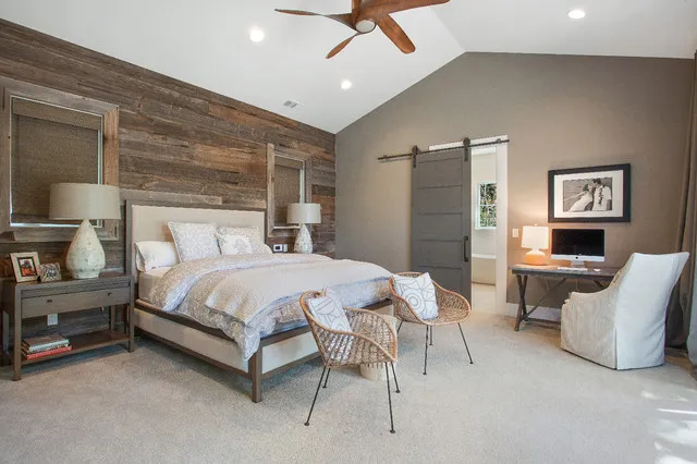 A pale bed stands against a timber feature wall with woven chairs at its foot and a desk nearby.
