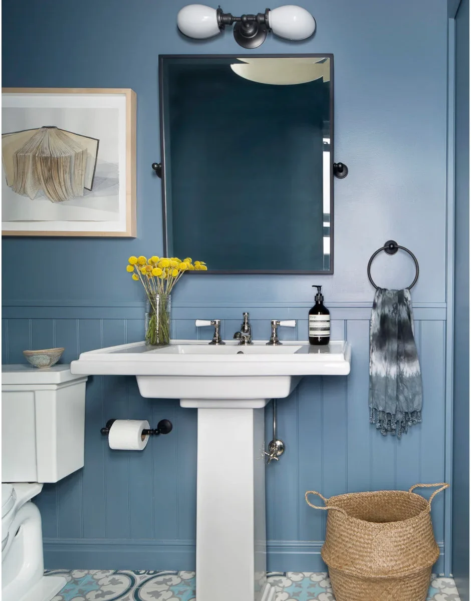 A dark round towel ring holds a patterned towel beside a white pedestal sink against blue paneled walls.