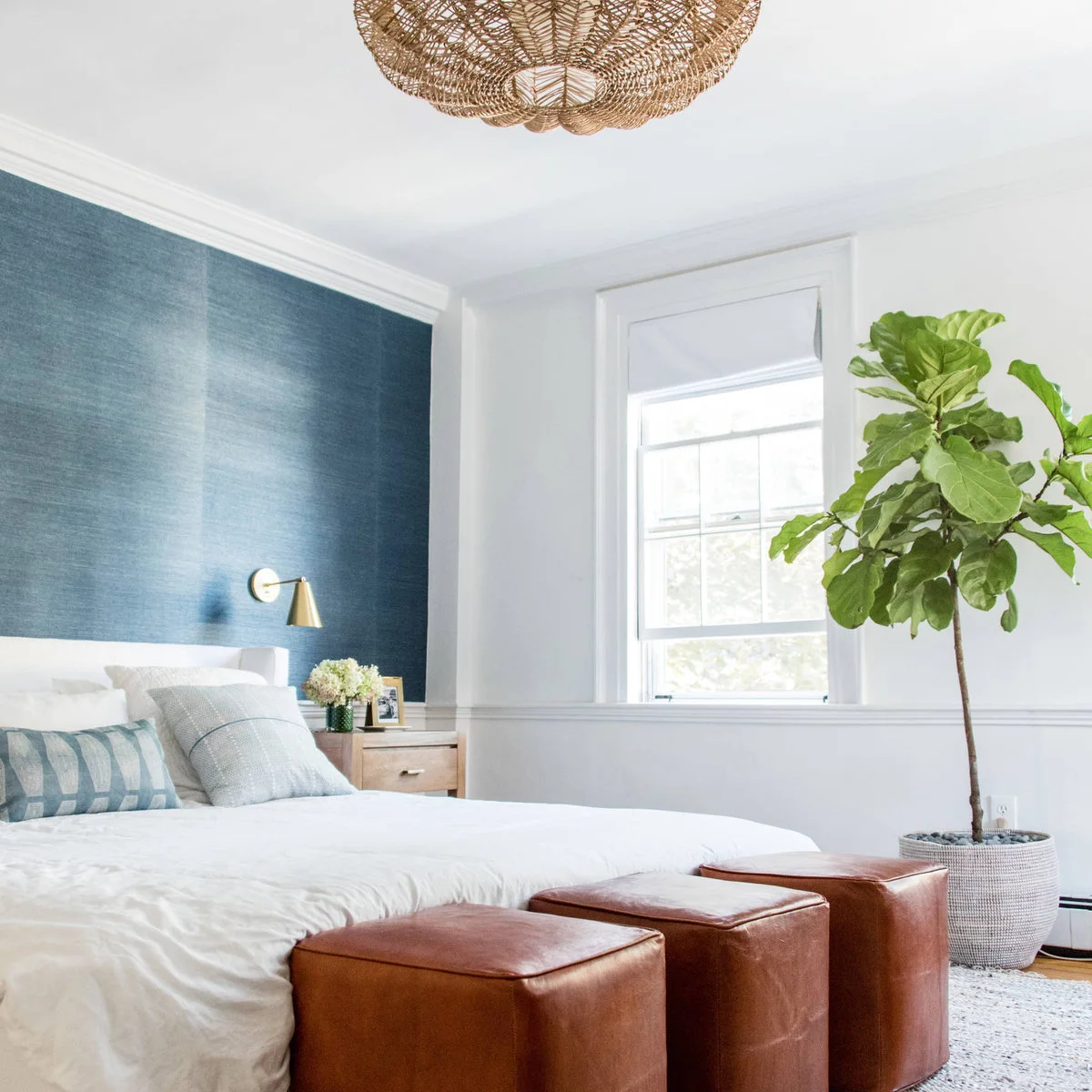 Blue textured accent wall behind a white bed with a brass-colored reading light and brown stools.