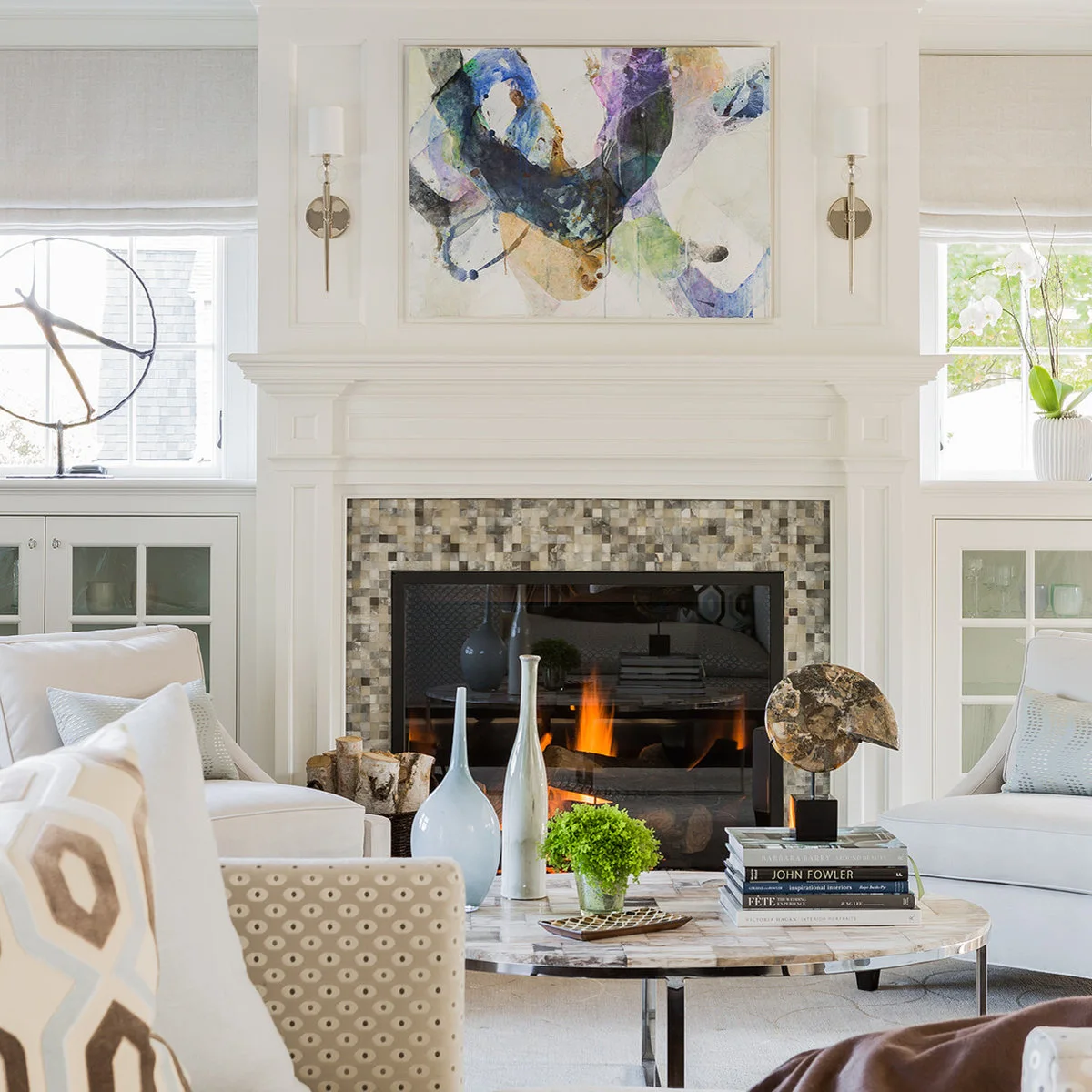 Two slender warm metal sconces with small white shades flank artwork above a white paneled fireplace.