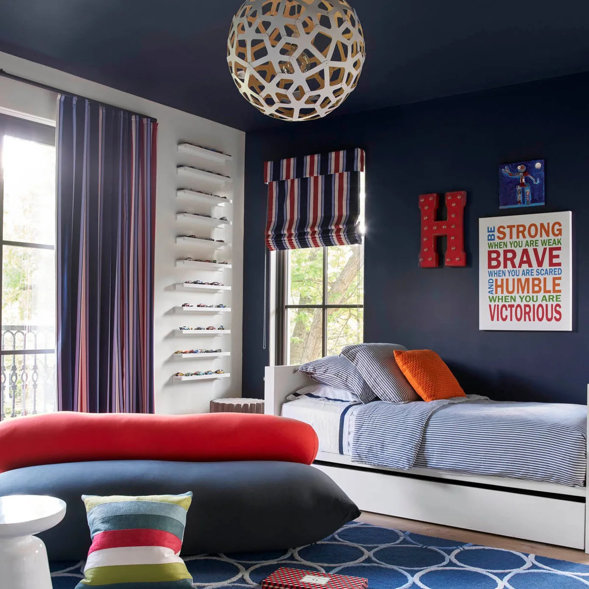 Navy boy’s bedroom with narrow toy-car display ledges, striped bedding and a curved lounge seat