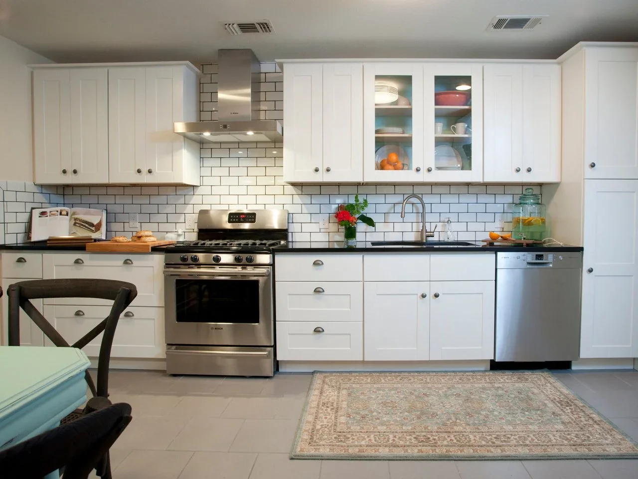A compact white kitchen has subway tiles with dark grout behind a range and sink above a black counter.