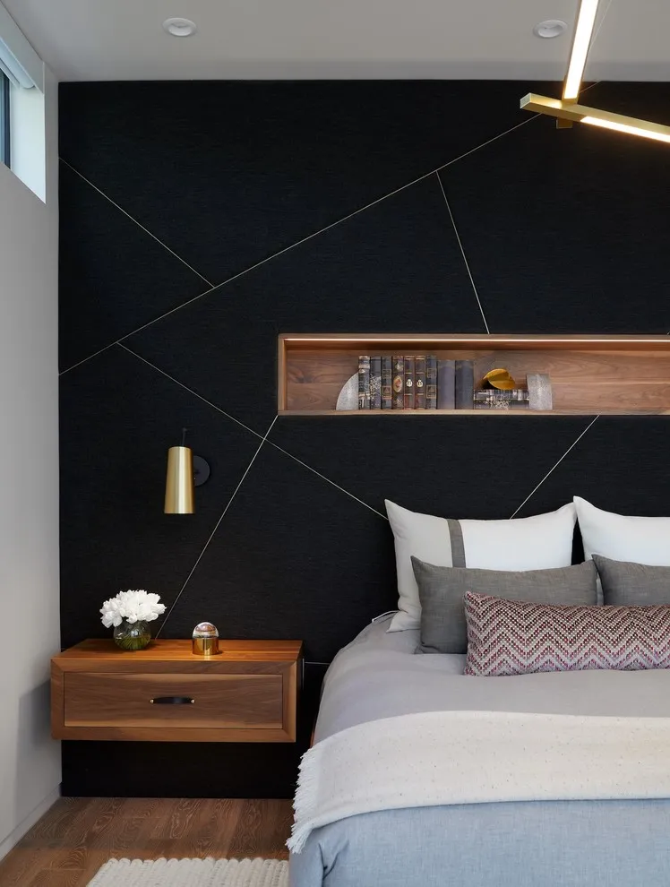 Fine diagonal lines cross a black wall behind a gray bed and timber shelf