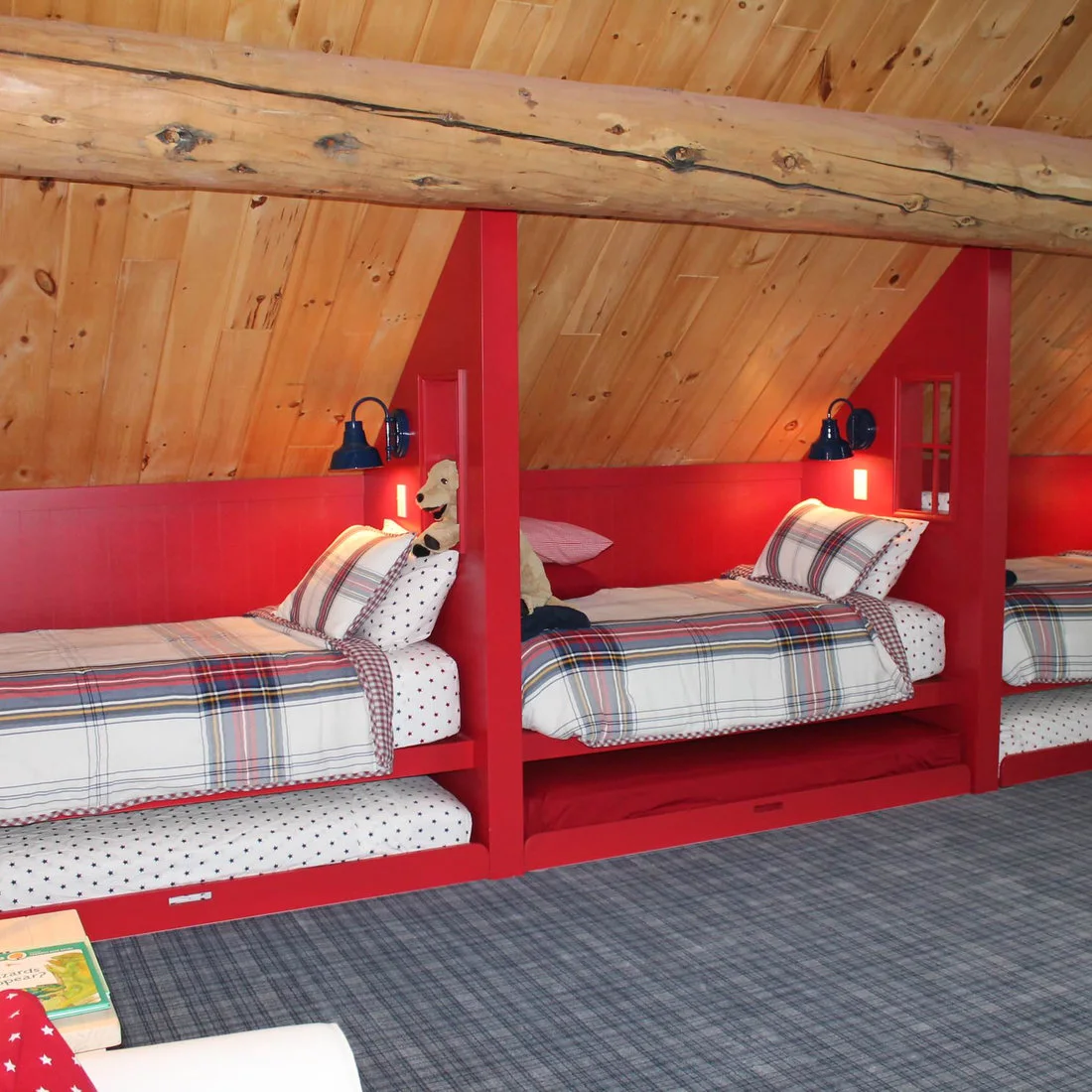 Red built in beds and trundle drawers beneath a timber slope with checked bedding and blue lamps