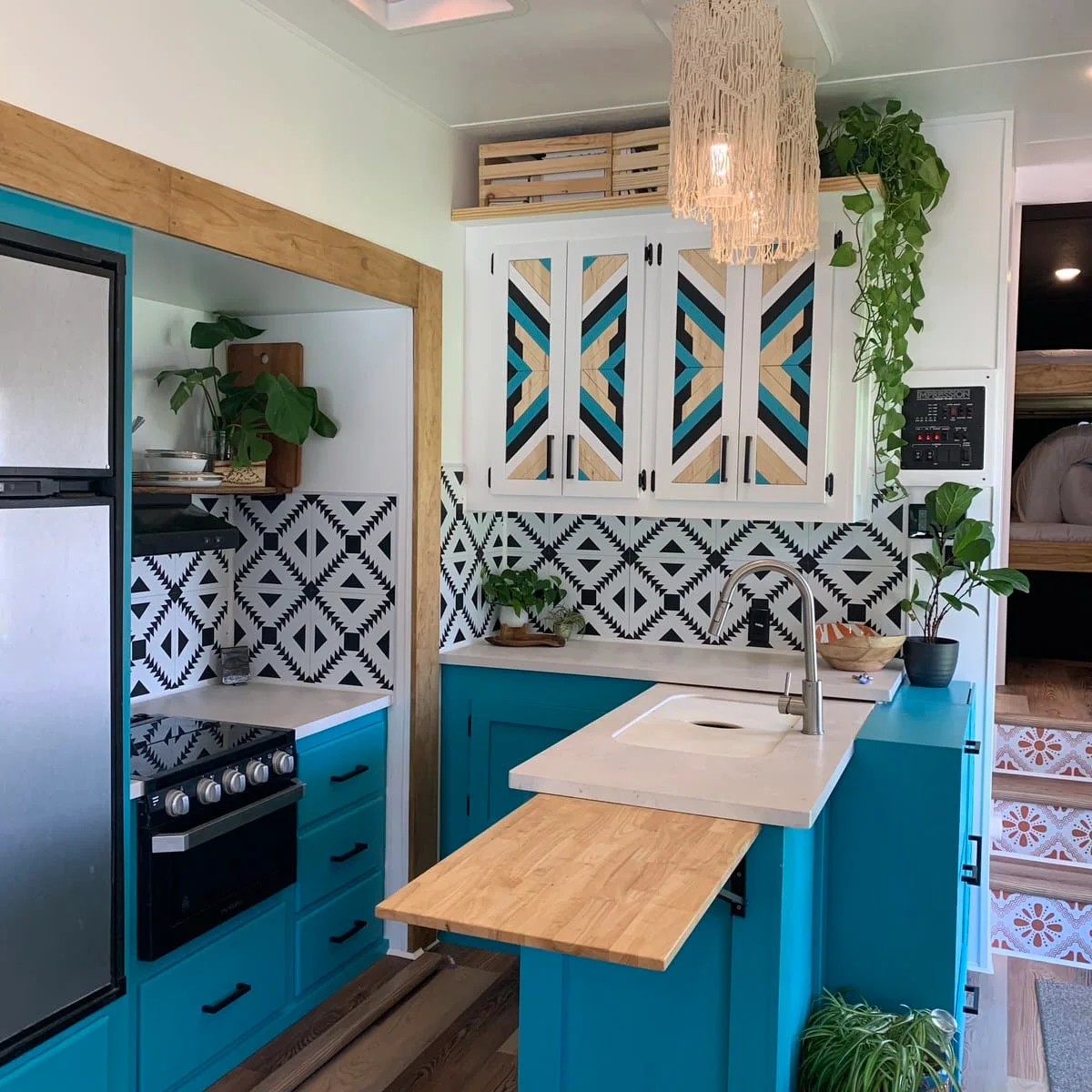 Turquoise RV kitchen with a wood counter extension on folding brackets and patterned upper cabinet fronts.