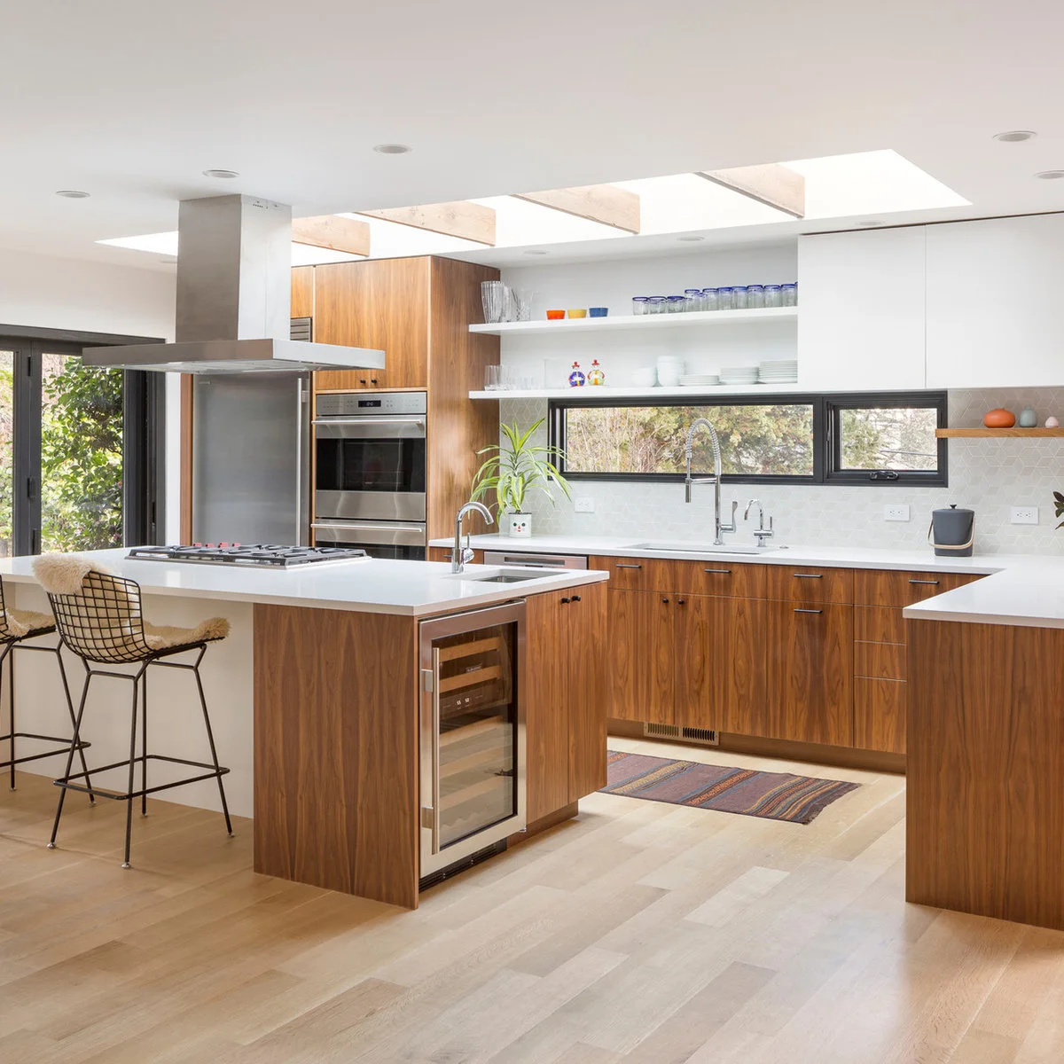 Wood lower cabinets and white uppers around a long low window above the sink, with a skylight and island hood.