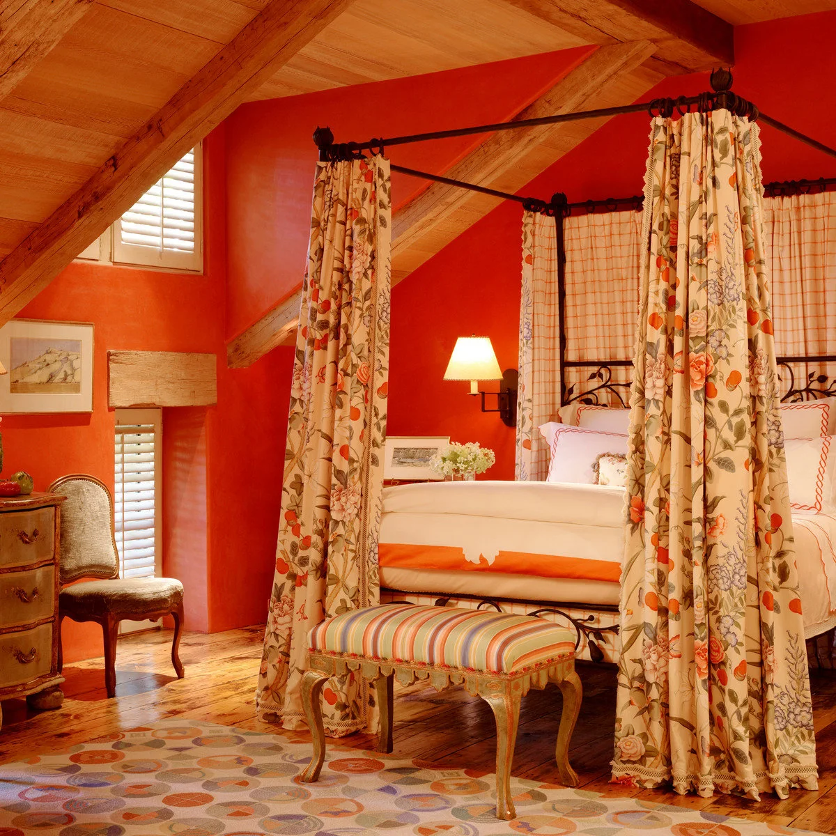 Orange bedroom with a dark canopy bed, floral bed curtains and a striped upholstered bench