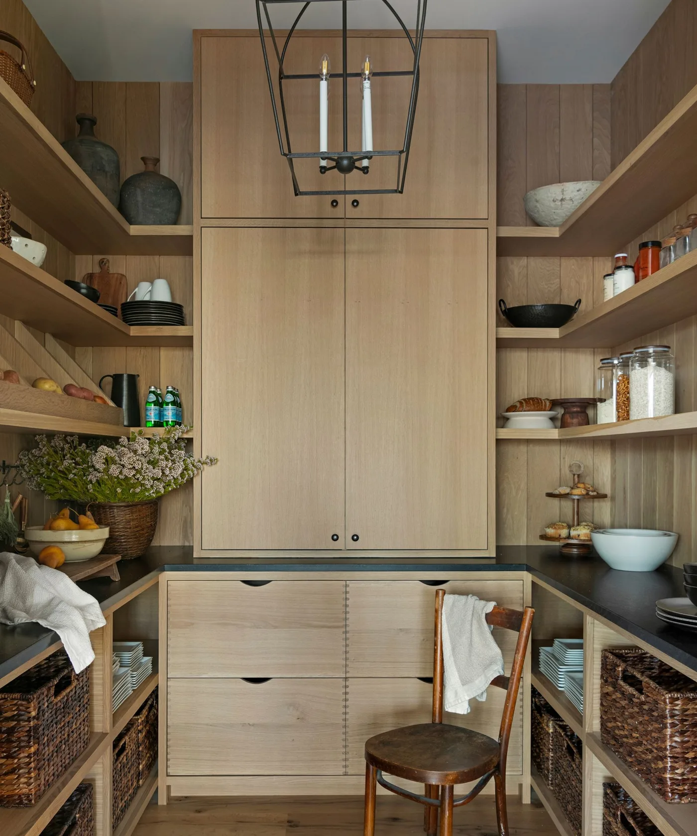Wood-lined country pantry with open shelves, central tall cupboard, dark counters and lower baskets