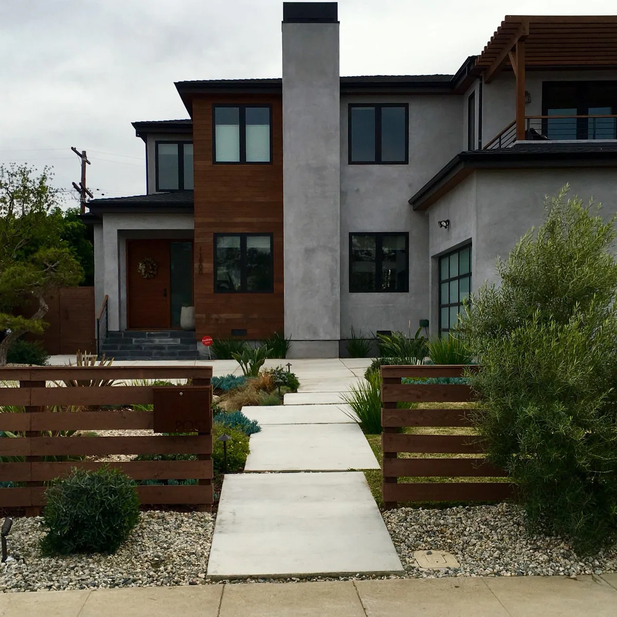 Two low horizontal wood fence sections frame a pale path leading toward a contemporary house entrance.