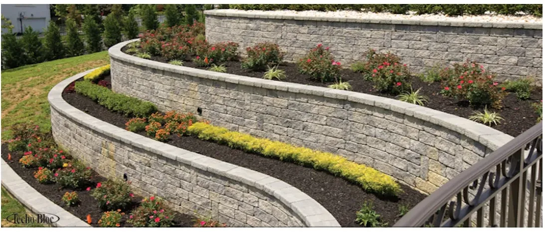 Three curved gray block retaining walls hold planted terraces with flowers and contrasting foliage.
