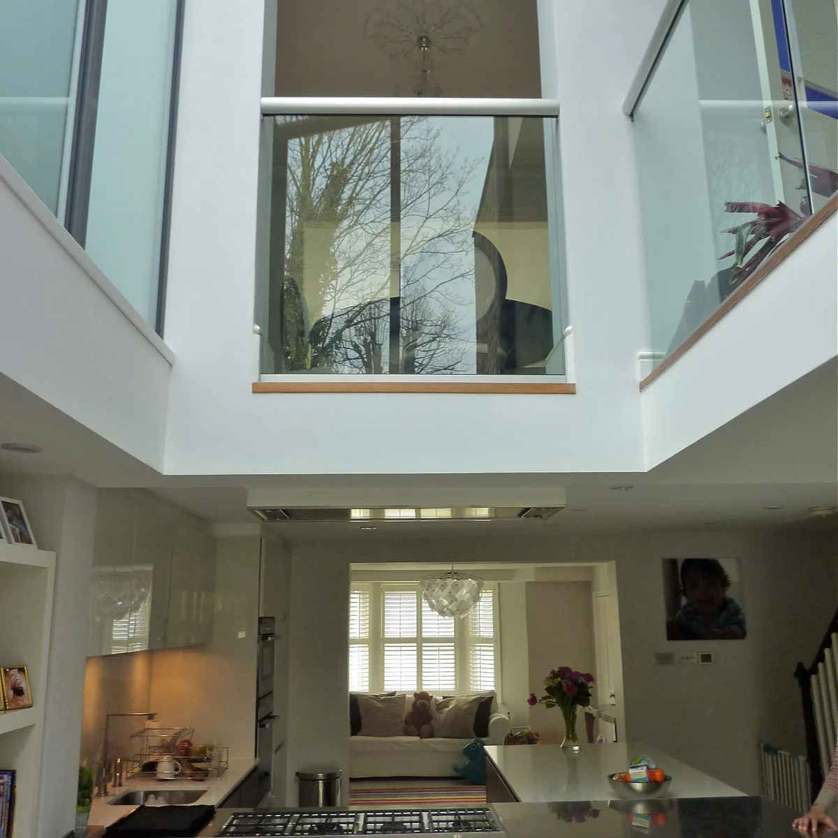 Terraced-house kitchen beneath a double-height opening with glazed barriers and a view into another sitting room