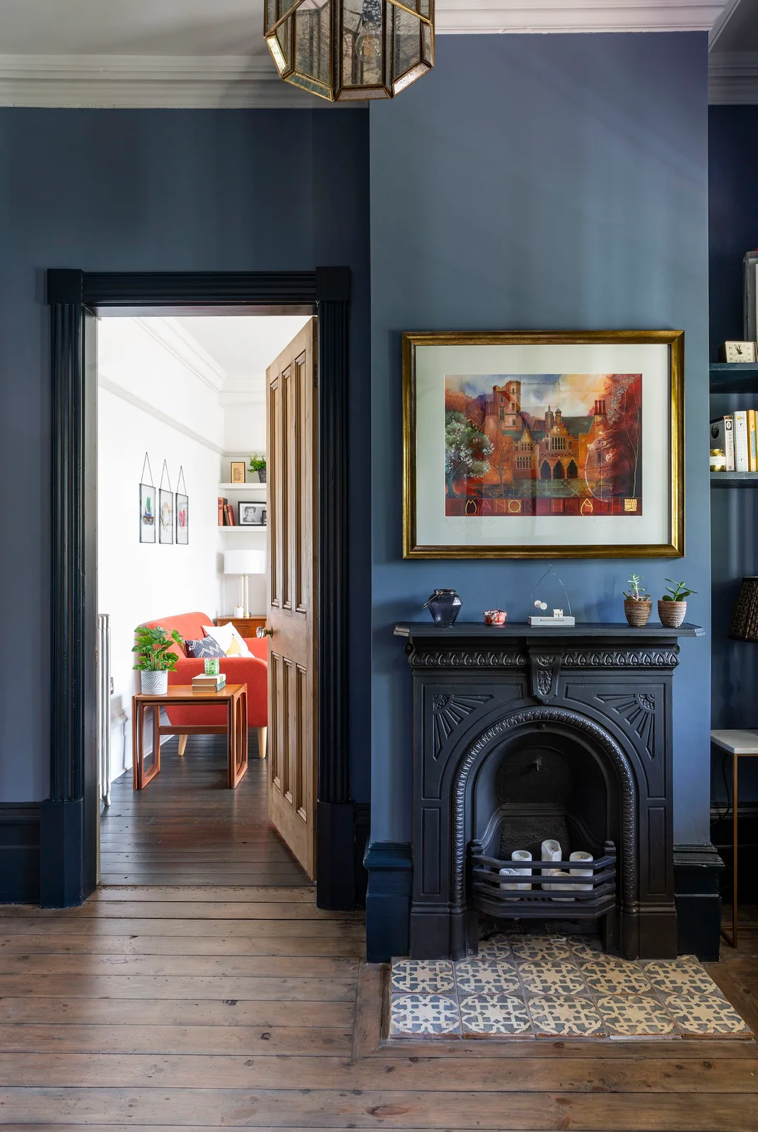 A dark ornate fireplace with a patterned hearth stands beside a doorway in a blue-walled hallway.