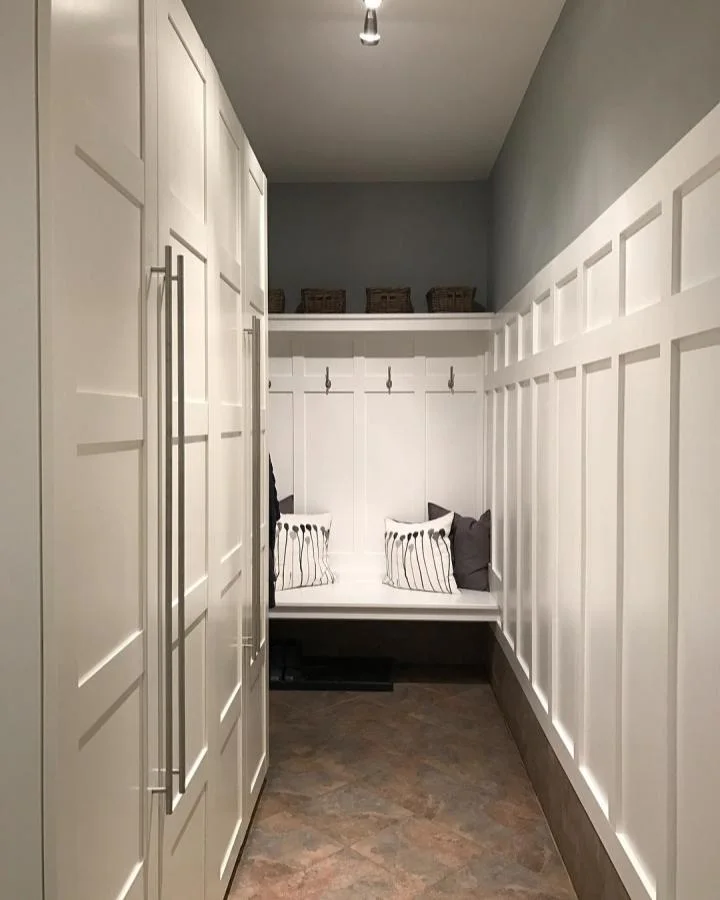 Narrow entryway with tall white wardrobes along one side and a small hook-and-seat area at the far end.