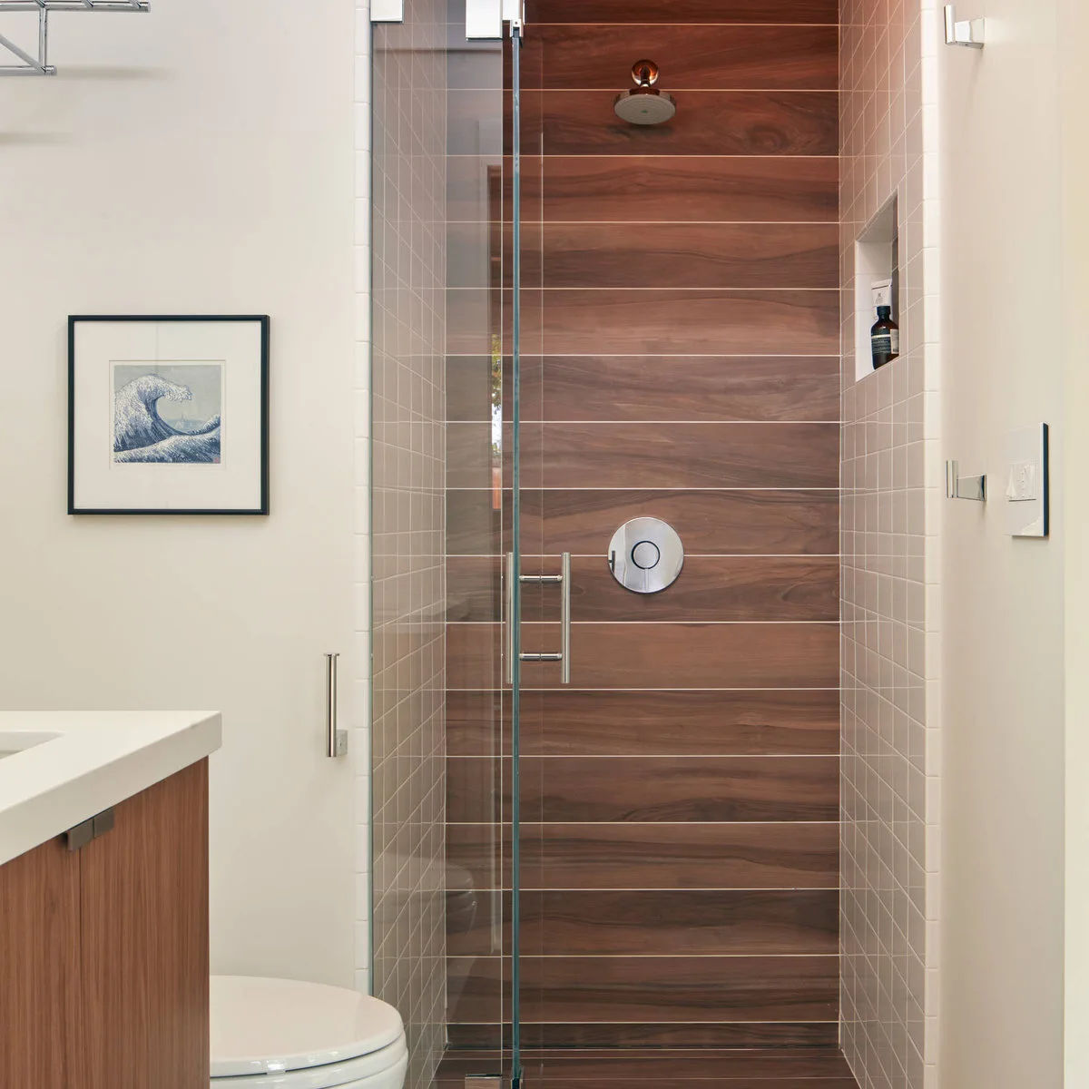 Small framed wave print on a dry wall beside a wood-toned shower enclosure