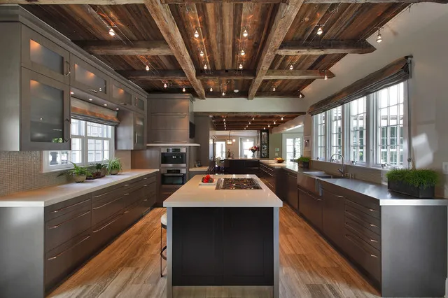 A black island stands between long timber cabinet runs beneath an exposed wood ceiling.