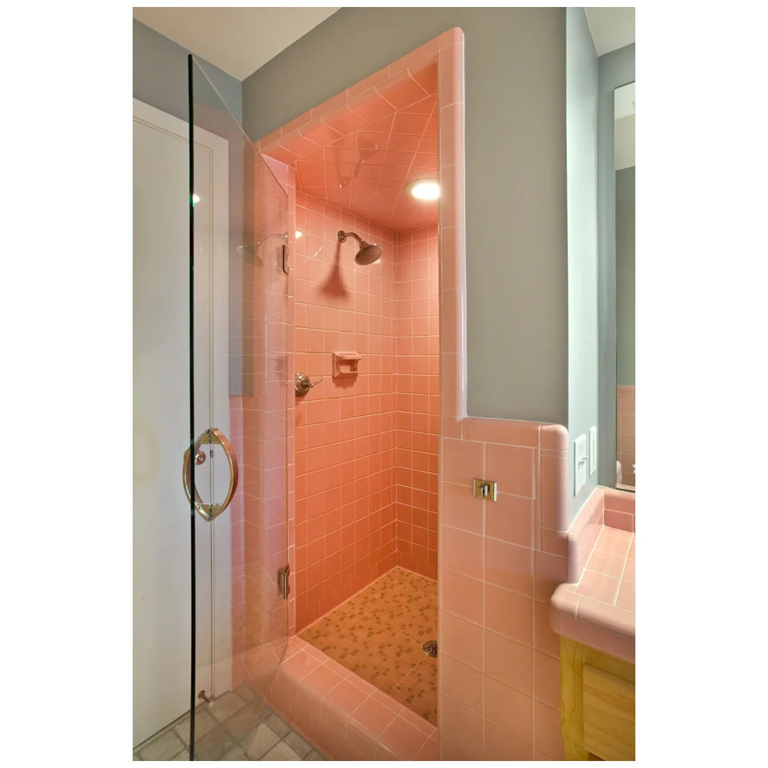 Pink tiles surround a shower and long vanity in a bathroom with gray upper walls and a patterned floor