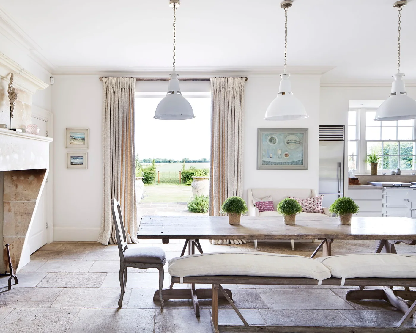 Cream patterned curtains around garden doors beside a wood table and white kitchen
