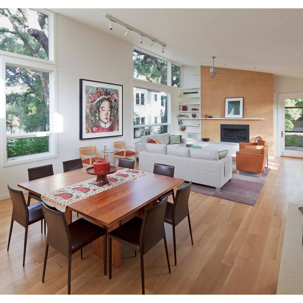 Long light room with a wooden dining table in the foreground, pale sofas on a patterned rug and an orange fireplace wall beyond.