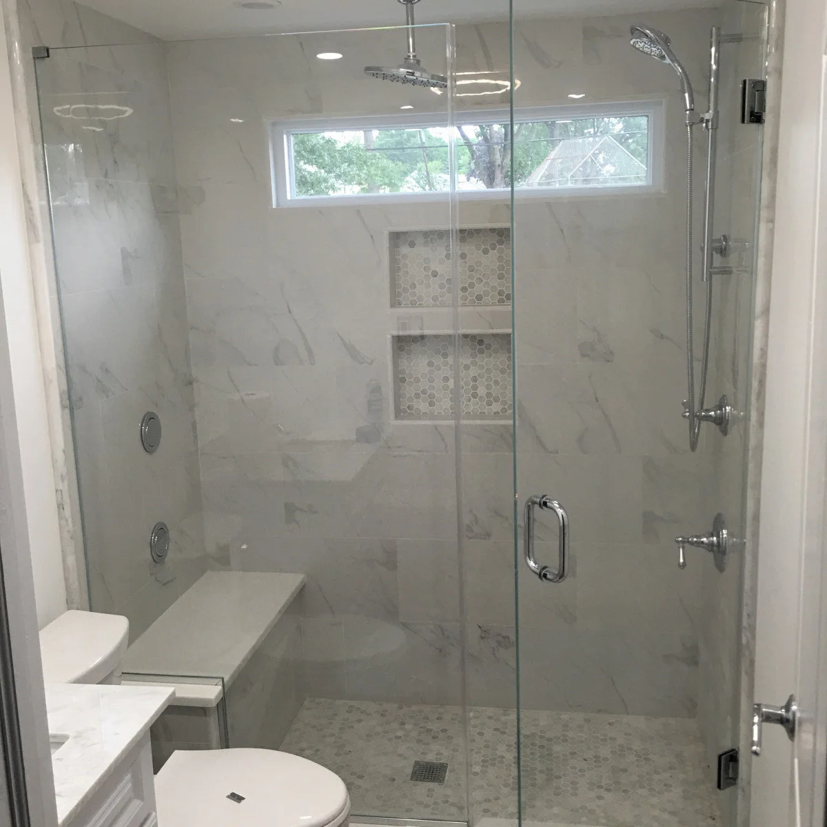 Glass shower with a wall-mounted folding seat and paired recessed shelves