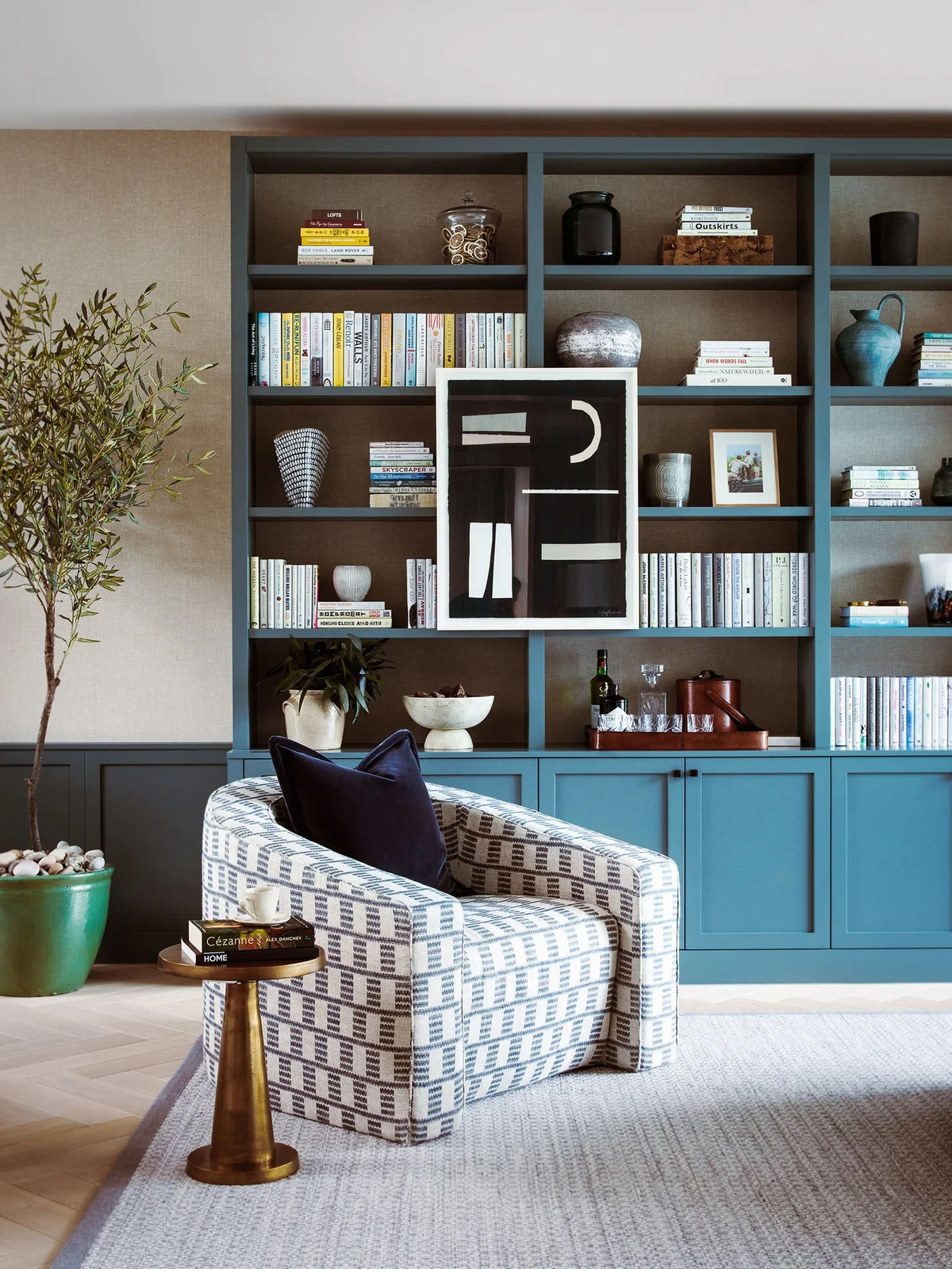 A blue fitted cabinet and open bookcase include a drinks tray, a pale plant pot and a raised bowl below a large black-and-white artwork.