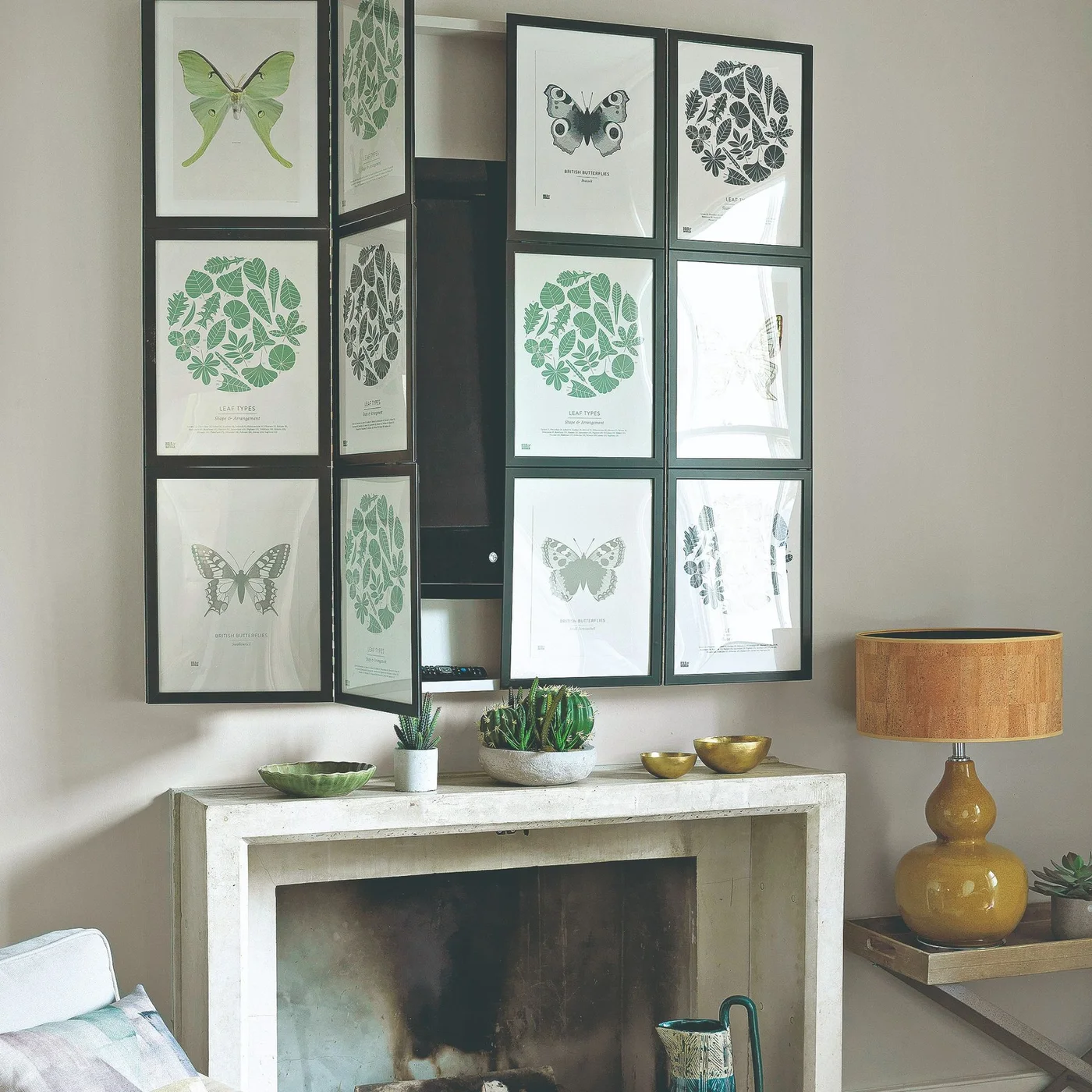 Framed botanical panels fold aside to reveal a television above a pale fireplace surround.