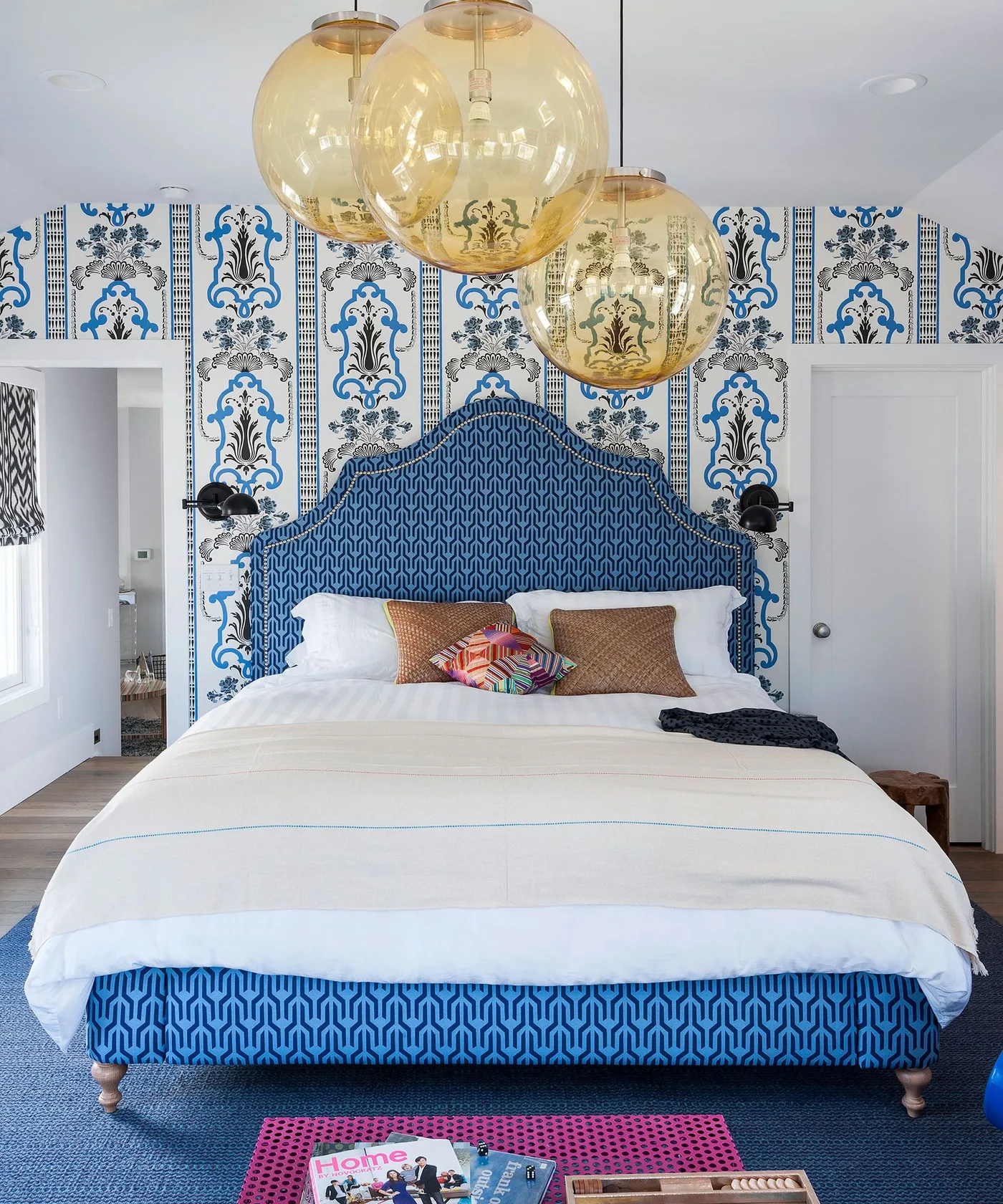 Blue patterned upholstered bed with graphic blue-and-white wallpaper and amber globe pendants.