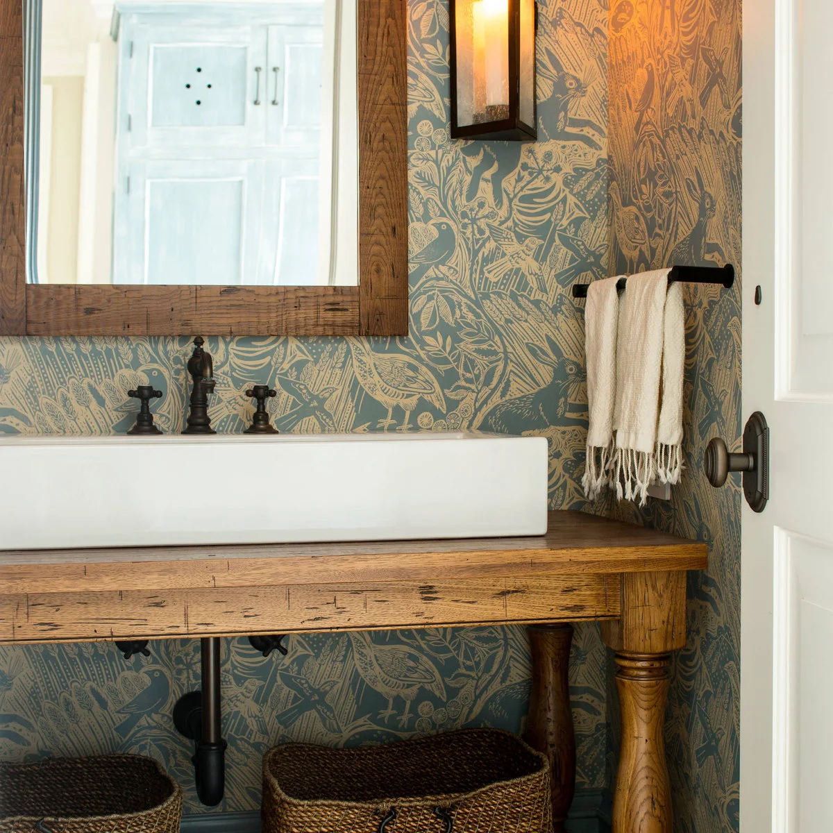 A short dark towel rail holds two pale fringed towels beside a rectangular vessel sink against blue and gold patterned wallpaper.