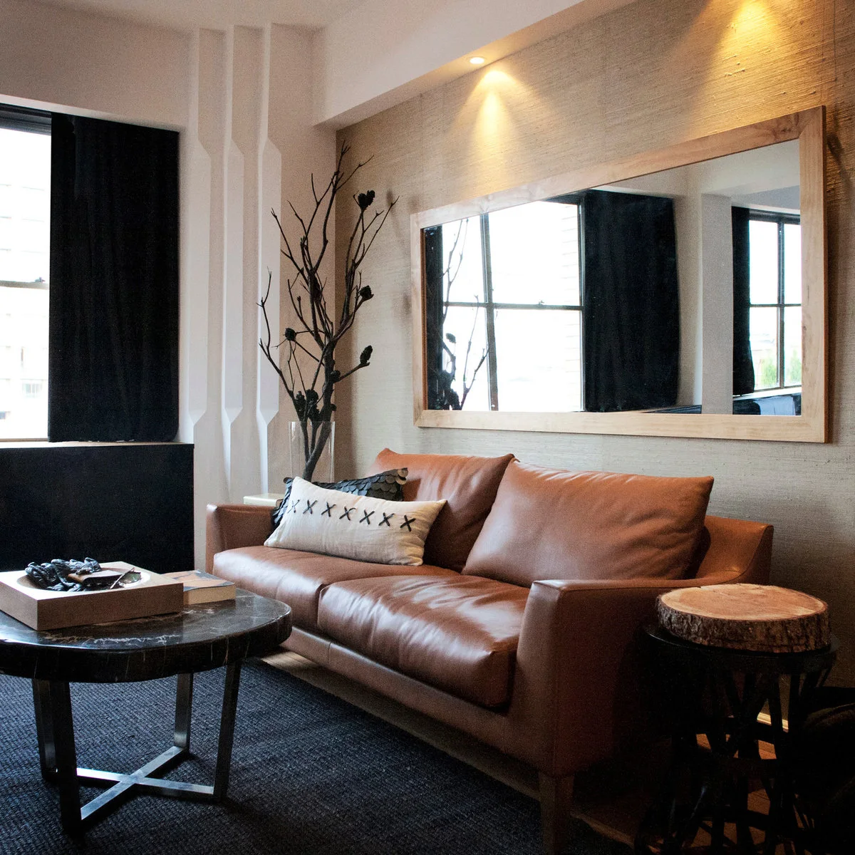Compact sitting area with tan sofa, dark curtains and a black round coffee table