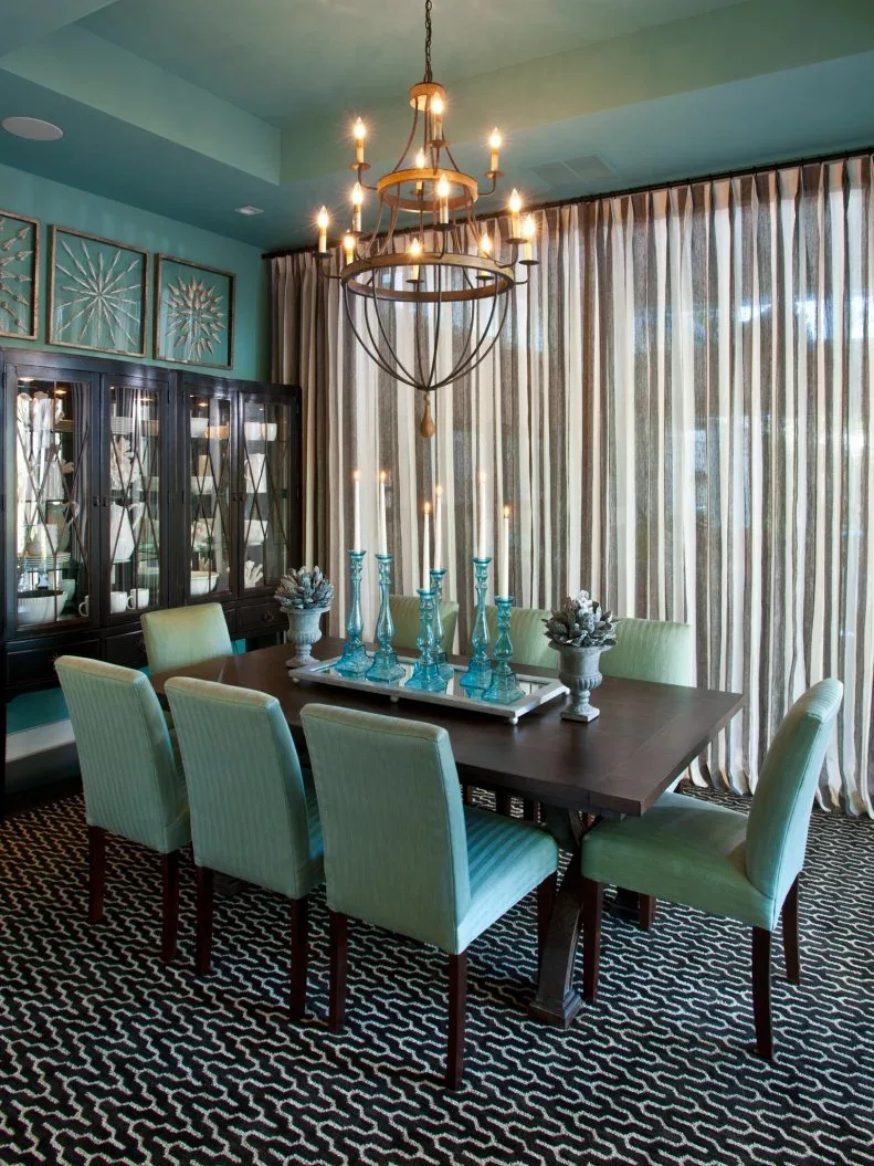 Dining room with blue walls and ceiling, dark wooden table and glazed cabinet, aqua upholstered chairs and striped curtains.