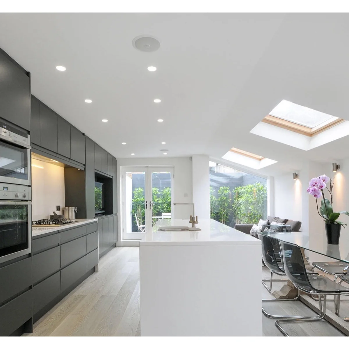 Terrace kitchen with gray cabinet wall, white island and rooflights above dining and seating space