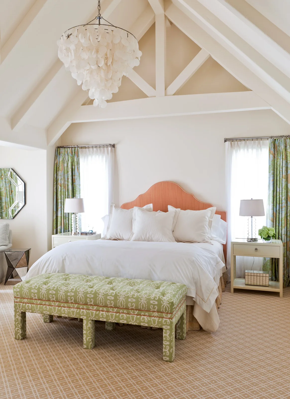 White bedroom with a coral curved headboard, green patterned bench and pale patterned curtains