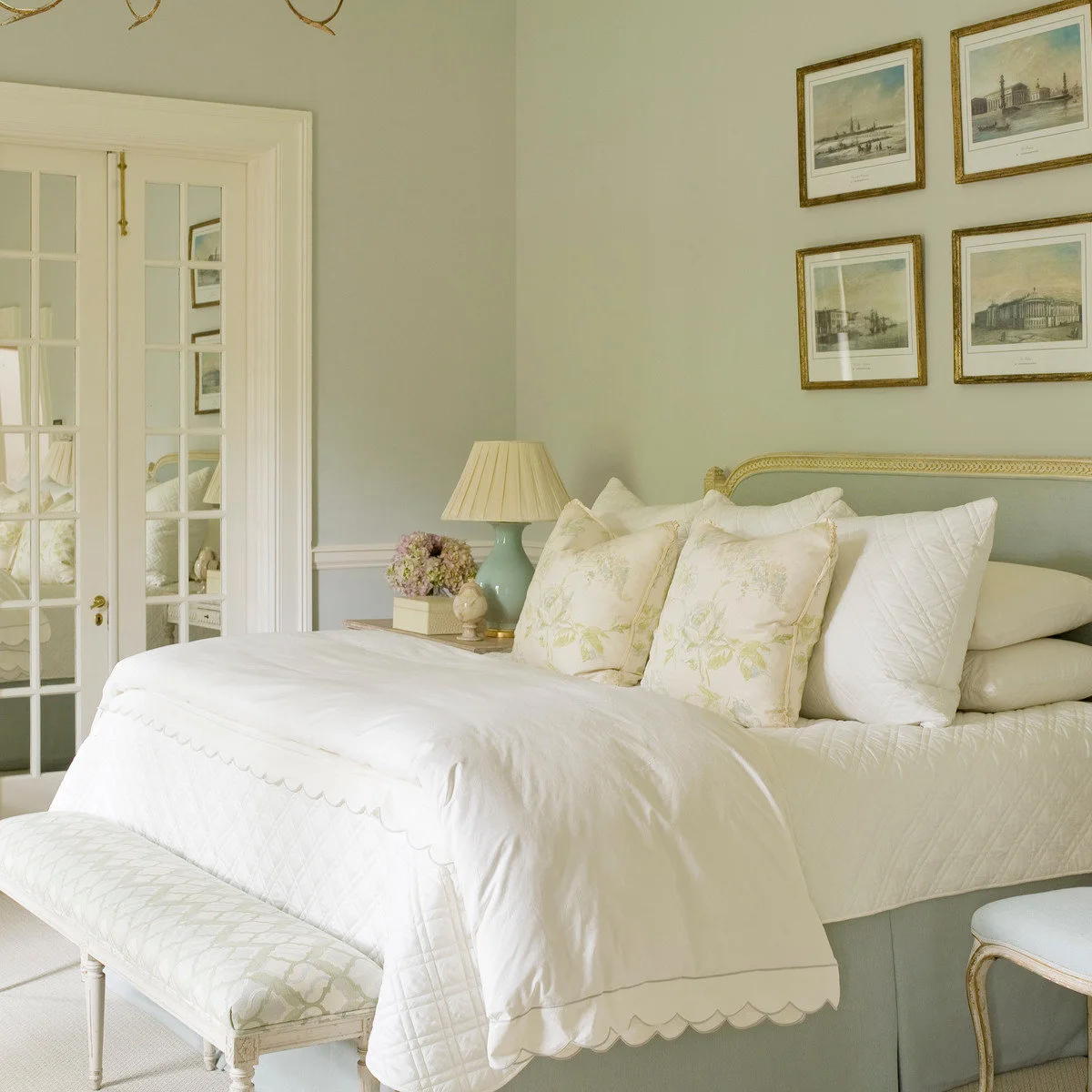 Traditional bedroom with pale green walls, cream scalloped bedding, floral cushions and a mint bedside lamp